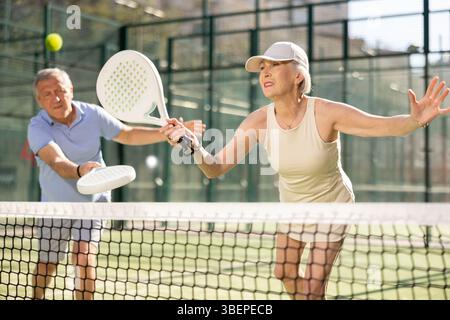 Uomo e donna anziani motivati che giocano a padel con il suo compagno di squadra in tribunale Foto Stock
