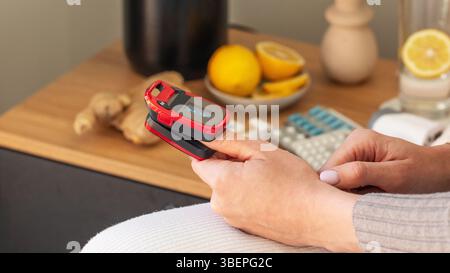Femmina caucasica che utilizza pulsossimetro rosso sul dito per il monitoraggio della salute a casa Foto Stock