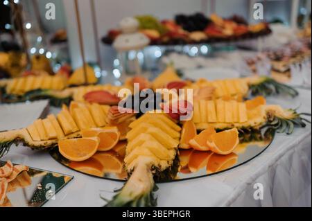 Un ricco e vibrante vassoio di frutta presentato su una superficie a specchio durante un evento, con mango a fette, arance, ananas, uva, e othe Foto Stock