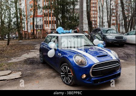 Una Mini Cooper blu decorata con palloncini azzurri e un orsacchiotto sul tetto è parcheggiata di fronte a un edificio, che celebra una nuova celebrità della baby car Foto Stock