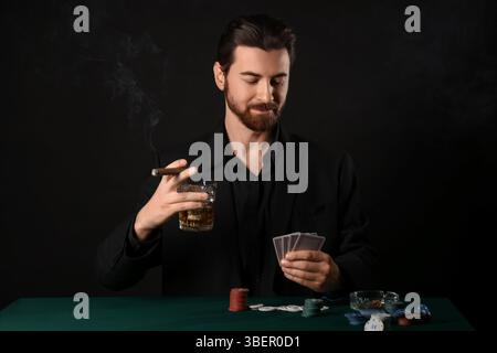 Bel giovane con whisky e sigaro che gioca a poker al tavolo del casinò Foto Stock