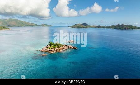 Una piccola isola rocciosa coperta di vegetazione si trova nel mezzo di ampie acque turchesi. Saint Pierre, Isole Curieuse. Seychelles. Foto Stock