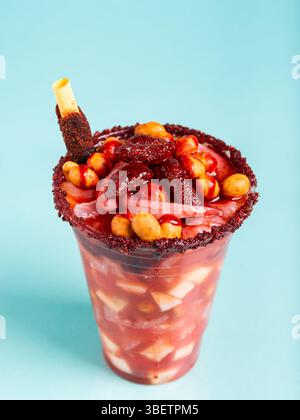 Un bicchierino pazzesco, una miscela di ingredienti dolci, salati e speziati isolati su sfondo blu. Spuntino tipico dal Messico. Foto Stock