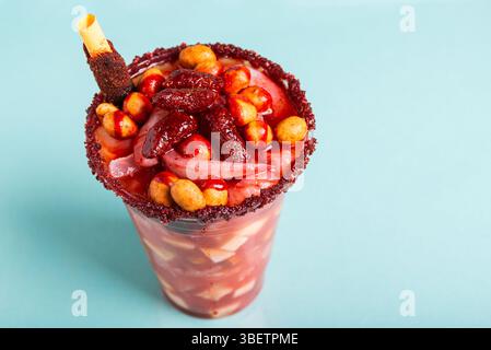 Un bicchierino pazzesco, una miscela di ingredienti dolci, salati e speziati isolati su sfondo blu. Spuntino tipico dal Messico. Foto Stock