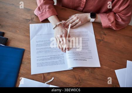 Persona che si concentra sulla revisione dei documenti finanziari alla scrivania di legno, indossando un orologio da polso. Diversi documenti e documenti si stanno diffondendo nell'area di lavoro, Foto Stock