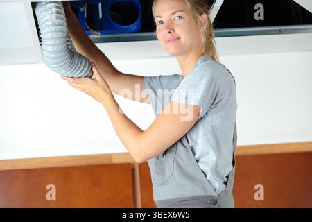 Lavoratore di sesso femminile che di montaggio del sistema di ventilazione a soffitto degli edifici Foto Stock