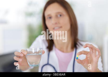 donna medico tiene un bicchiere con acqua e dà pillole Foto Stock