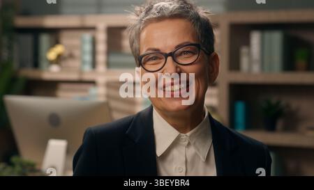 Donna d'affari caucasica donna d'affari anziana ridendo sorridente gioia divertimento in ufficio lavoratrice matura pensata vecchio datore di lavoro che guarda il sorriso della macchina fotografica Foto Stock