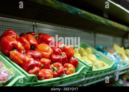 Vari peperoni colorati disposti in casse di plastica verde al mercato di alimenti freschi. Le verdure come i peperoni rossi, gialli e d'arancia sono in mostra Foto Stock