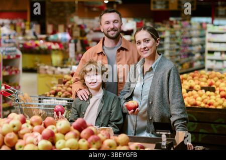 Famiglia che acquista mele fresche al negozio di alimentari, in attesa della sezione prodotti e sorridendo per la macchina fotografica. Ritratto di una famiglia che si diverte a trascorrere momenti di qualità insieme Foto Stock