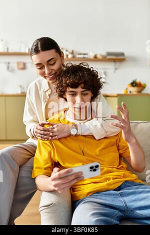 Una coppia si siede insieme su un comodo divano, condividendo momenti di risate mentre usa lo smartphone. Foto Stock