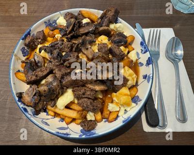 Poutine di manzo e funghi servite su un tavolo rustico nell'ambiente del ristorante Foto Stock