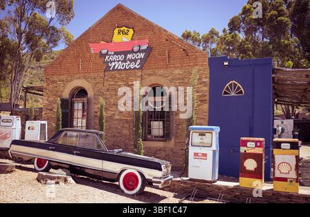 Un'auto d'epoca e colorate pompe a gas si trovano fuori dal Karoo Moon Motel sulla Route 62 in Sud Africa, circondati da segnaletica retrò e caratteri rustici Foto Stock