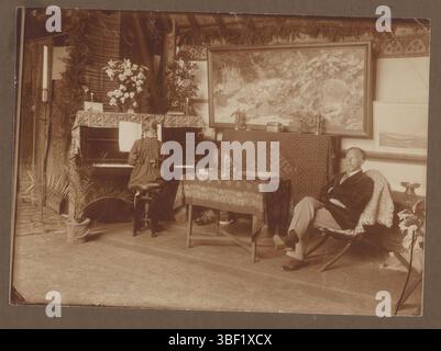Ragazza al pianoforte, uomo seduto nell'interno della sedia, ca. 1916, destra sotto (recto) - in inchiostro nero, ragazza che suona al pianoforte a sinistra nella foto, uomo con barba seduto in poltrona a destra. Grande dipinto sullo sfondo con motivi vegetali. Dallo stesso album: RP-F-00-6024., fotografia, foto, foglio di album, foto, MEI 1916, altezza 129 mm, larghezza 178 mm, altezza 220 mm, larghezza 299 mm, fotografo, 1916-05, primo quarto del xx secolo, carta fotografica, carta fotografica, cartone, stampa in argento gelatina, stampa gelatina di sviluppo Foto Stock