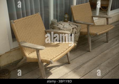 Sedie a sdraio in rattan intrecciato accanto ad un rustico tavolino in legno su un ponte di legno Foto Stock