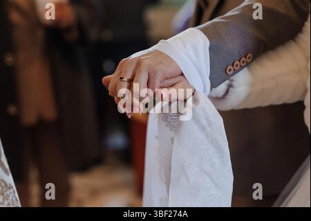 Foto ravvicinata di una sposa e di uno sposo che si tengono per mano, in vista delle fedi nuziali, ambientata in una chiesa, catturando la tenerezza e l'emozione dei loro voti Foto Stock