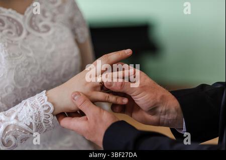 Foto ravvicinata di uno scambio di anelli nuziali, che mette in risalto le mani dello sposo mettendo con cura un anello d'oro sul dito della sposa adornato con d Foto Stock
