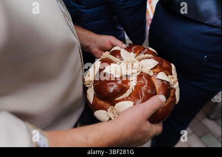 Uno scatto ravvicinato che cattura il momento in cui una sposa e uno sposo tengono in mano un pane polacco Korowaj splendidamente decorato, adornato con intricati disegni di grano e del Foto Stock