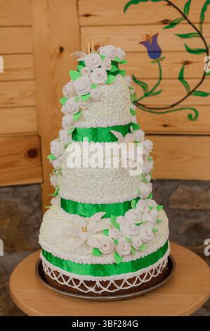 Una splendida torta nuziale a quattro piani è il punto focale, riccamente decorata con delicate decorazioni di rose bianche e vivaci dettagli verdi del nastro, presen Foto Stock