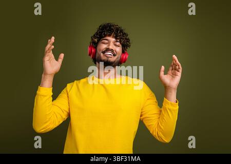 Giovane uomo che indossa le cuffie per ascoltare la musica con un'espressione gioiosa, che mostra felicità e relax su un sottofondo informale Foto Stock