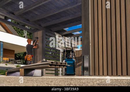 Un lavoratore esperto sta installando l'apparecchio di illuminazione in una struttura esterna contemporanea utilizzando vari strumenti. La luce del giorno aumenta l'attività A. Foto Stock