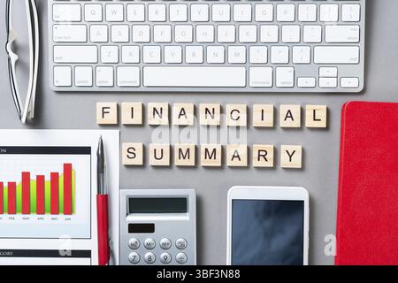 Concetto di riepilogo finanziario con lettere su cubi di legno. Durata residua del luogo di lavoro in ufficio con le forniture. Disporre la superficie grigia piatta con la tastiera del computer e. Foto Stock