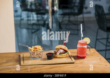 Delizioso hamburger di manzo con patatine fritte e una bevanda rinfrescante servita sul tavolo del ristorante Foto Stock