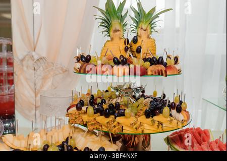 Un vassoio di frutta a due livelli splendidamente organizzato presenta un variopinto assortimento di ananas, uva, more, pesche e frutta a fette, stile Foto Stock