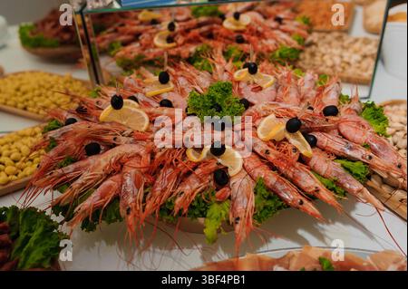 Una splendida disposizione di gamberetti, olive e spicchi di limone è splendidamente presentata su un grande piatto in un sontuoso buffet, che presenta deliziosi piatti Foto Stock