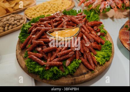 Un vivace e abbondante antipasto con salsiccia a fette, gamberi, noci varie e salsa cremosa disposta su un tavolo da portata in legno per una gioia Foto Stock