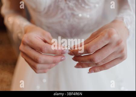 Uno scatto ravvicinato presenta una sposa che esamina delicatamente un anello di fidanzamento con diamanti scintillanti, indossa uno splendido abito da sposa in pizzo bianco, catturando un Foto Stock