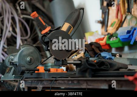 Una potente sega a taglio in metallo taglia una barra in acciaio in un ambiente di officina disordinato, con guanti di sicurezza visibili e un'estetica industriale scura Foto Stock