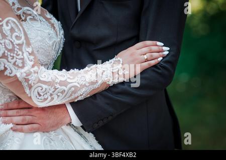 Uno scatto ravvicinato mostra una coppia di sposi che abbraccia, con particolare attenzione alle loro fedi nuziali e agli intricati dettagli in pizzo dell'abito della sposa, raffigurante Foto Stock