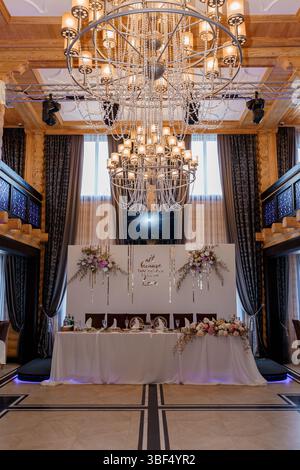 Splendido tavolo da nozze con un cartello "tutto a causa dell'amore" e disposizione floreale in una grande sala da ballo con pannelli in legno e un luccicante ch Foto Stock