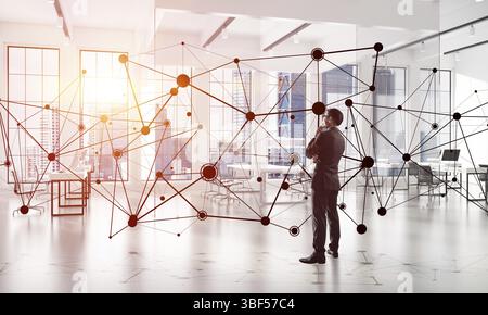 Imprenditore elegante in un ufficio moderno interiore e sociale il concetto di connessione. I supporti misti Foto Stock