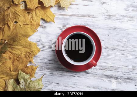 Composizione autunnale piatta con tazza di tè nero e foglie autunnali gialle. Concetto di pausa del tè. Bevande calde giace su una scrivania in legno vintage con b Foto Stock