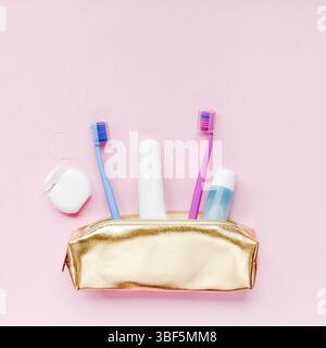 Igiene dei denti e prodotti oral dental care in Golden Travel kit borsa cosmetica su sfondo color rosa pastello con spazio copia. Tubo bianco di toothpa Foto Stock
