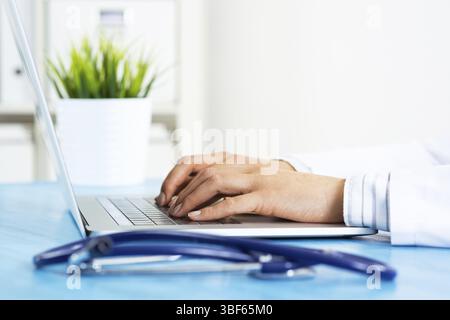 Terapeuta femminile che digita sulla tastiera del laptop. Medico in uniforme medica che lavora con il computer alla scrivania. Tecnologia moderna nell'esame e nella diagnosi Foto Stock