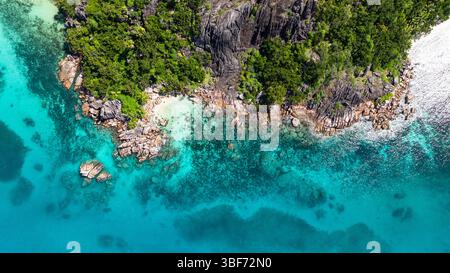 Grandi massi di granito incontrano le vibranti acque turchesi, con una piccola e isolata spiaggia di sabbia annidata tra vegetazione lussureggiante. Curieuse, Seychelles. Foto Stock