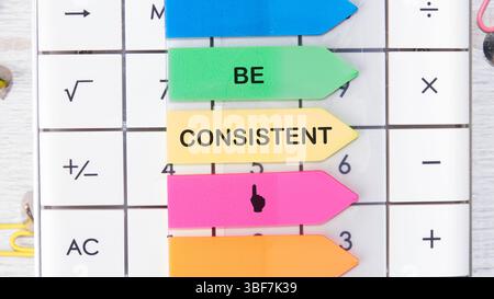 Testo del concetto aziendale ESSERE COERENTI messaggi motivanti sono posizionati sulla calcolatrice su adesivi luminosi. Foto Stock