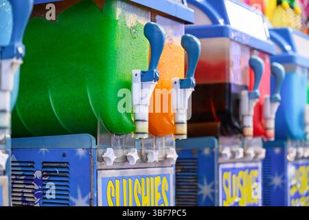 macchine per slushie commerciali al carnevale, con bevande colorate verdi e arancioni surgelate Foto Stock