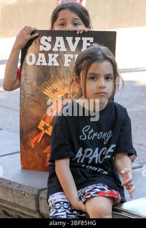 Due ragazzi ascoltano le canzoni dei nativi vengono eseguite prima della marcia verso il tribunale distrettuale nel Civic Space Park nel centro di Phoenix. Apache Stronghold, una coalizione di Apache e altri popoli indigeni, ha presentato una mozione di emergenza alla corte distrettuale federale per impedire al governo di trasferire il loro sito sacro ancestrale, Oak Flat, alla risoluzione Copper prima che la Corte Suprema decida se ascoltare il caso. Arizona, Stati Uniti. Foto Stock