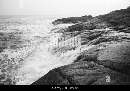 Seascape bianco e nero con onde che si infrangono sulla costa rocciosa Foto Stock