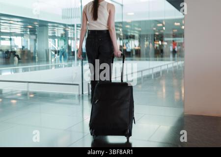 Giovane donna che cammina attraverso il terminal dell'aeroporto con la valigia. Concetto di viaggio indipendente, stile di vita moderno e mobilità fluida. Foto in movimento Foto Stock