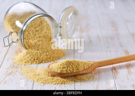 Couscous organico in paletta in legno e vasetto in vetro su un tavolo leggero, messa a fuoco selettiva. Foto Stock