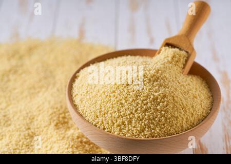 I couscous crudi sono sparsi in una ciotola di legno da vicino. Foto Stock