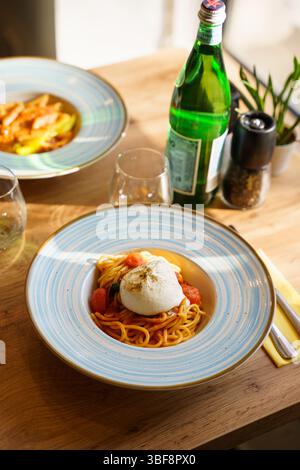 Primo piano di spaghetti conditi con burrata intera, serviti in un ricco sugo di pomodoro con pomodori ciliegini e basilico fresco. Un gourmet italiano Foto Stock