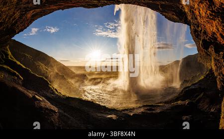 La vista della cascata Seljalandsfoss dall'interno della cascata con un incredibile tramonto in una tranquilla area paesaggistica del cerchio d'Oro in Islanda Foto Stock