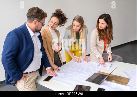 Architetti maschili e femminili con un progetto sul tavolo che discute e pianifica un nuovo progetto in un ufficio moderno Foto Stock