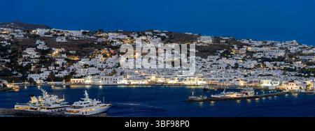 Il porto di Mykonos di notte, la Grecia, il vivace porto di Mykonos, brulicante di barche da pesca, yacht eleganti e vivaci caffetterie sul lungomare. Gli edifici imbiancati brillano sotto il sole dell'Egeo, mentre la brezza salata trasporta il ronzio della conversazione e il profumo del mare, una scena senza tempo dove tradizione ed energia cosmopolita si incontrano su questa iconica isola greca. Mykonos è un'isola del gruppo delle Cicladi nel Mar Egeo. Foto Stock
